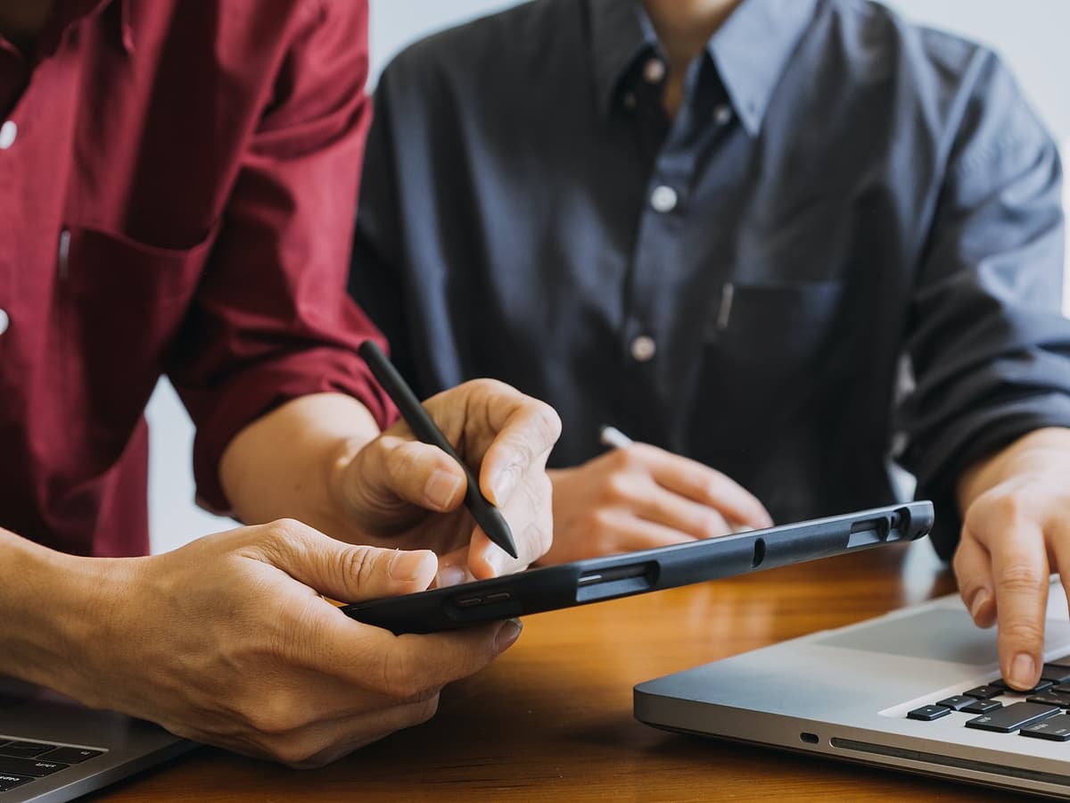 Two individuals collaborating on a laptop and tablet, engaged in productive work.