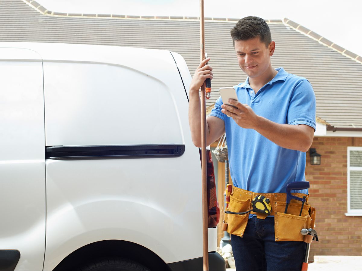 Plumber in blue shirt looking at phone while on job site next to his white job van