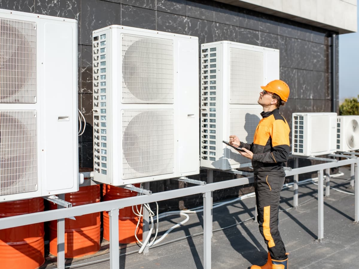 A man in an orange hard hat stands beside air conditioning units, ensuring their proper installation and maintenance.