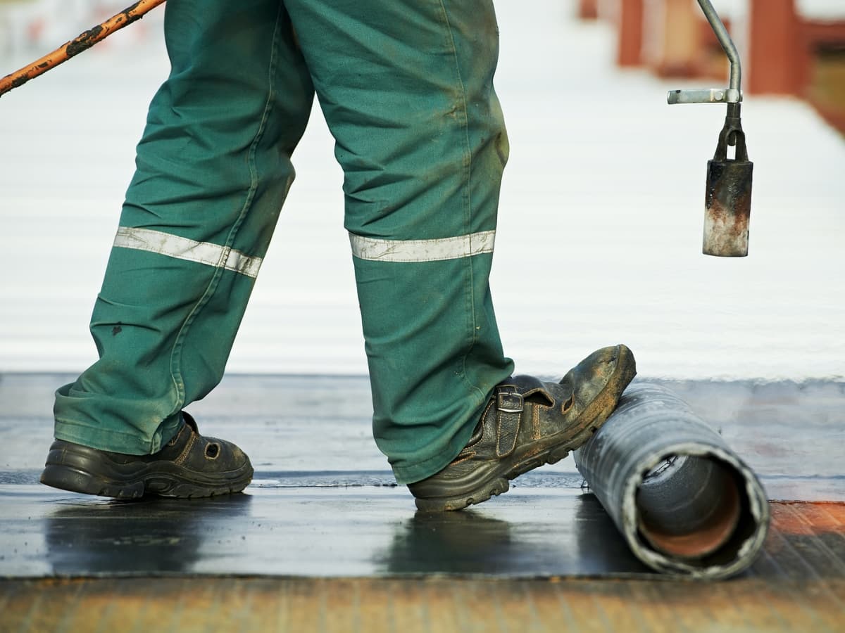 Worker in green pants and boots installing flat roof.