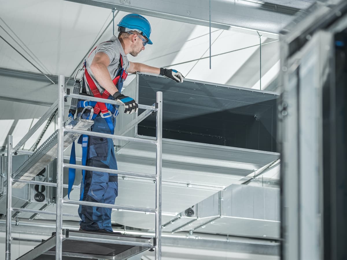 HVAC worker on ladder in commercial building.