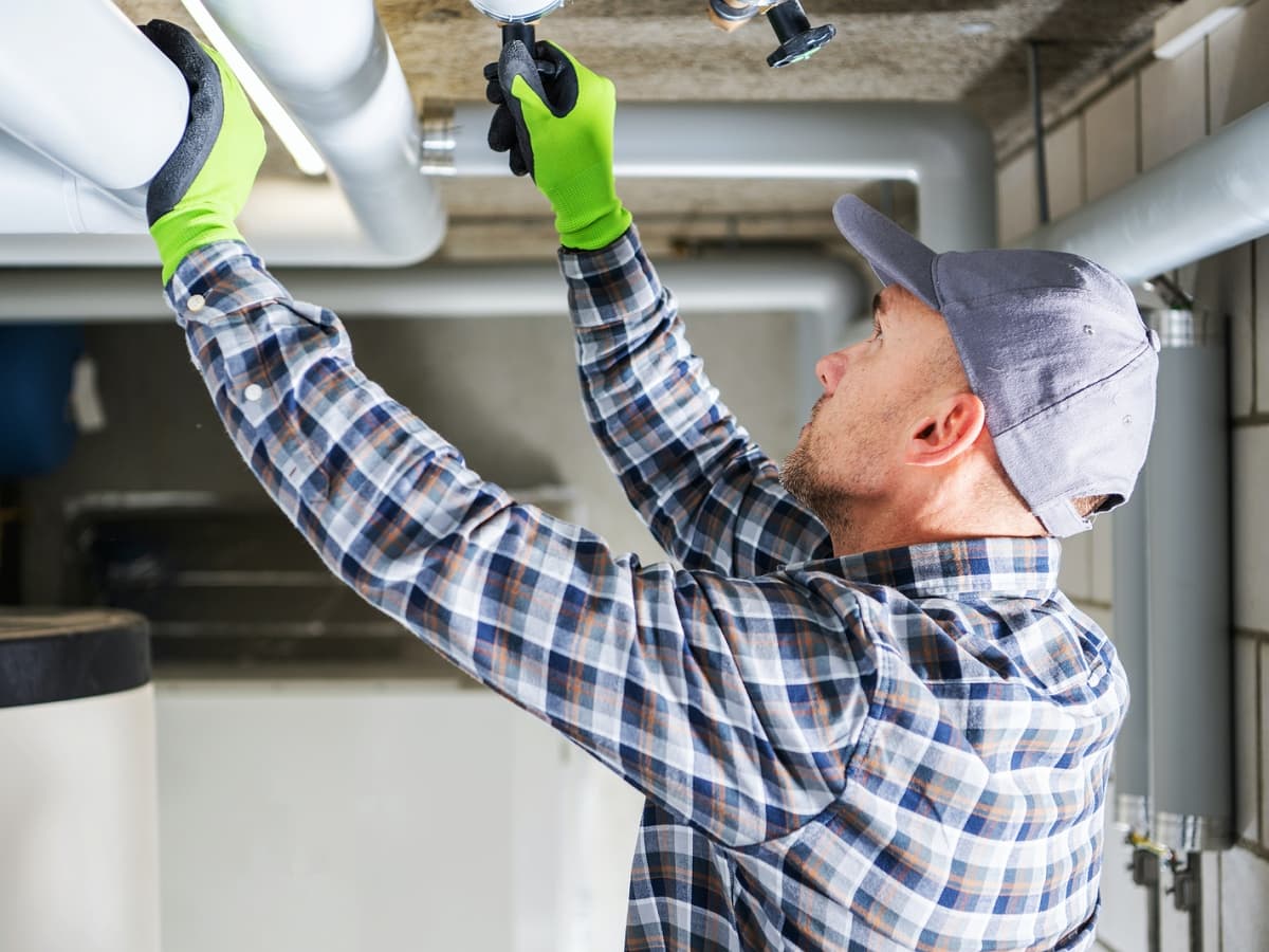 Man in plaid shirt and hat fixing pipe.