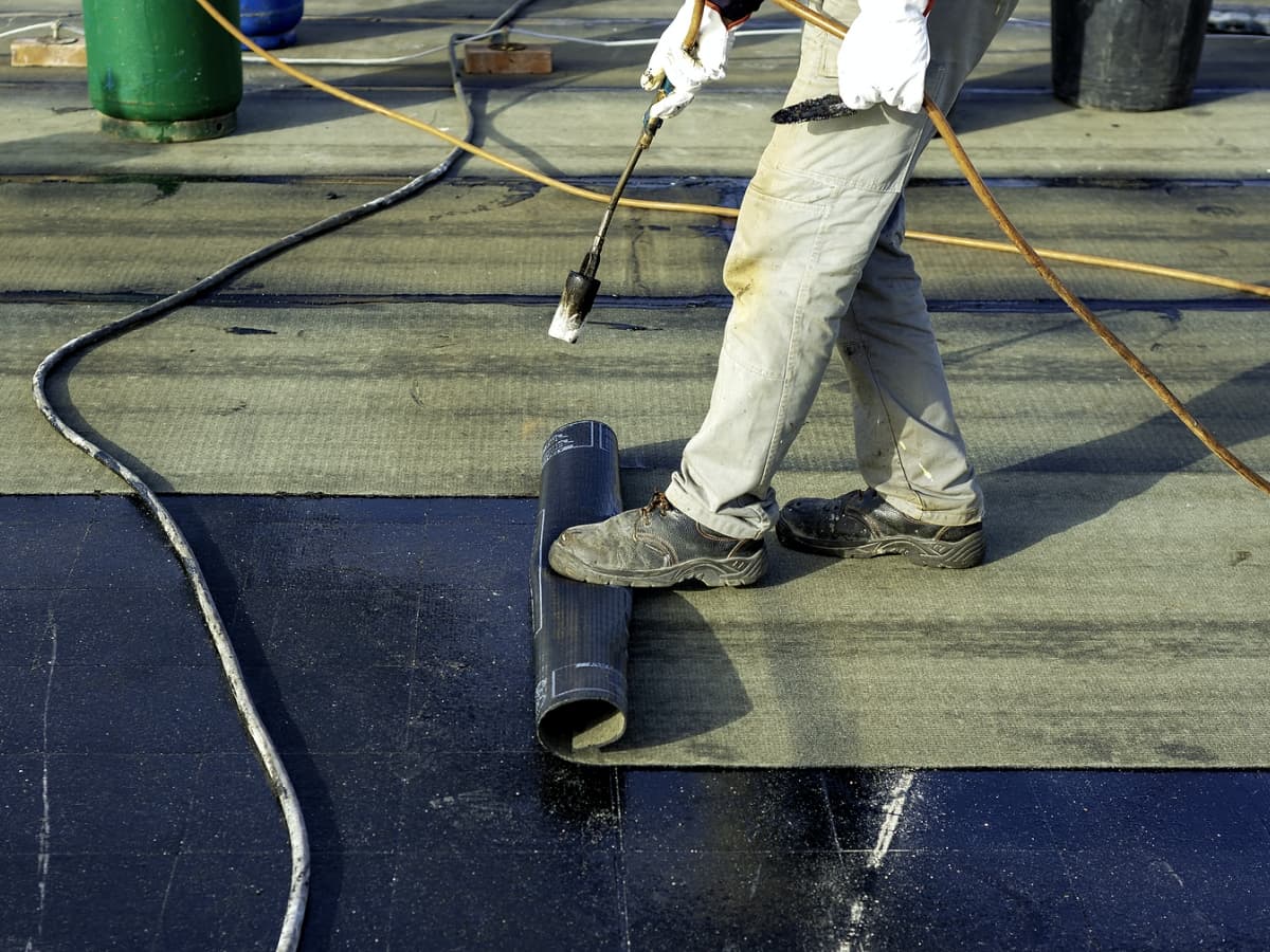 A roofer installing a black material on a flat roof.
