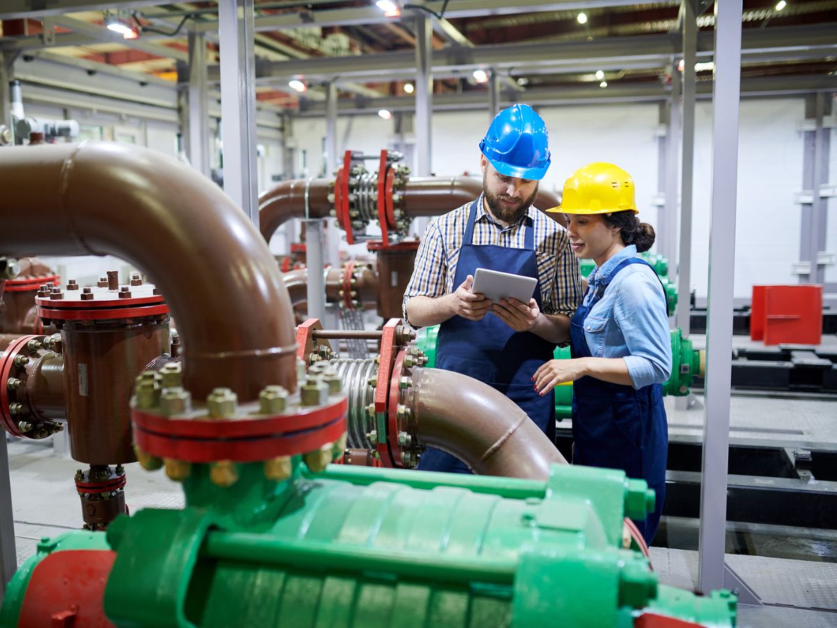 Two industrial plumbing contractors consult a tablet with field management software.