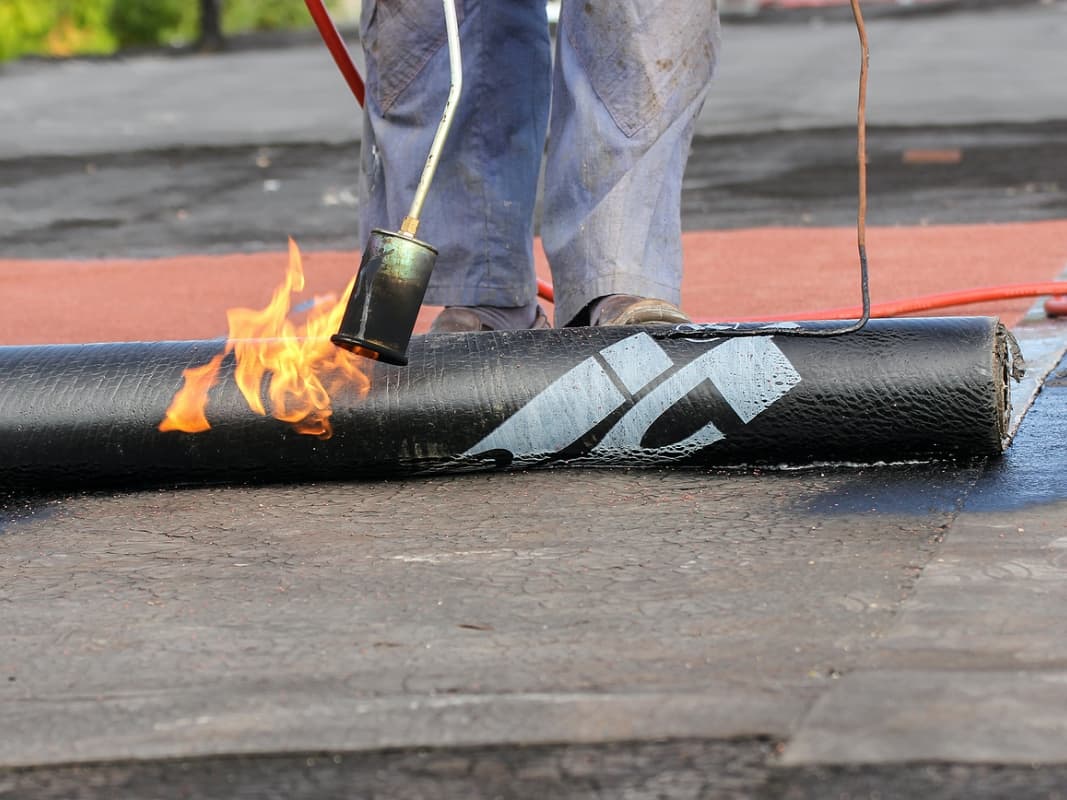 Roofing installation on flat roof by contractor with flame tool.