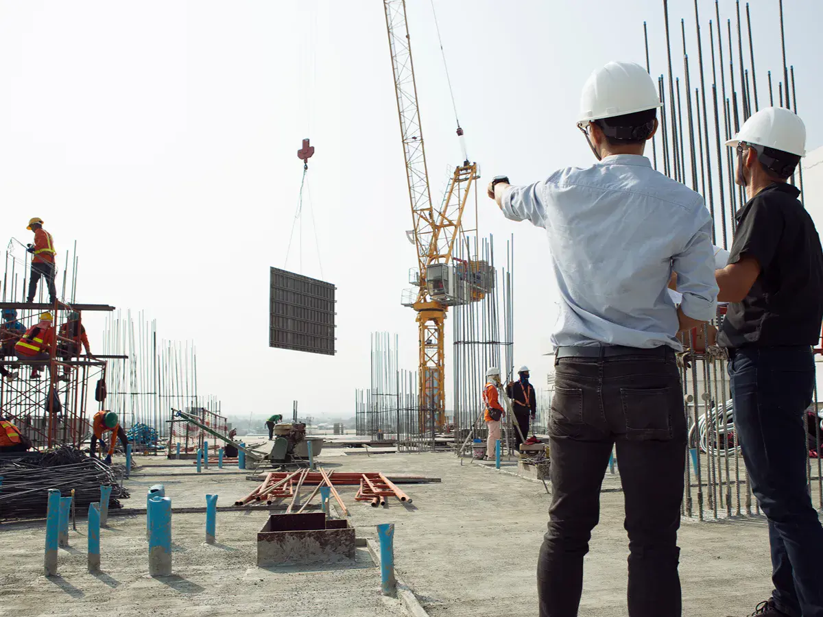 Two people standing outside looking at a construction site and wearing hard hats.