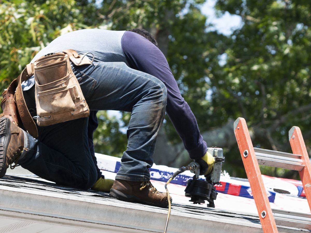 Roofing worker on a new job attaching shingles atop a roof