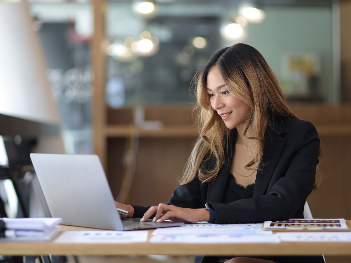 A woman sitting at a desk and typing on a laptop.